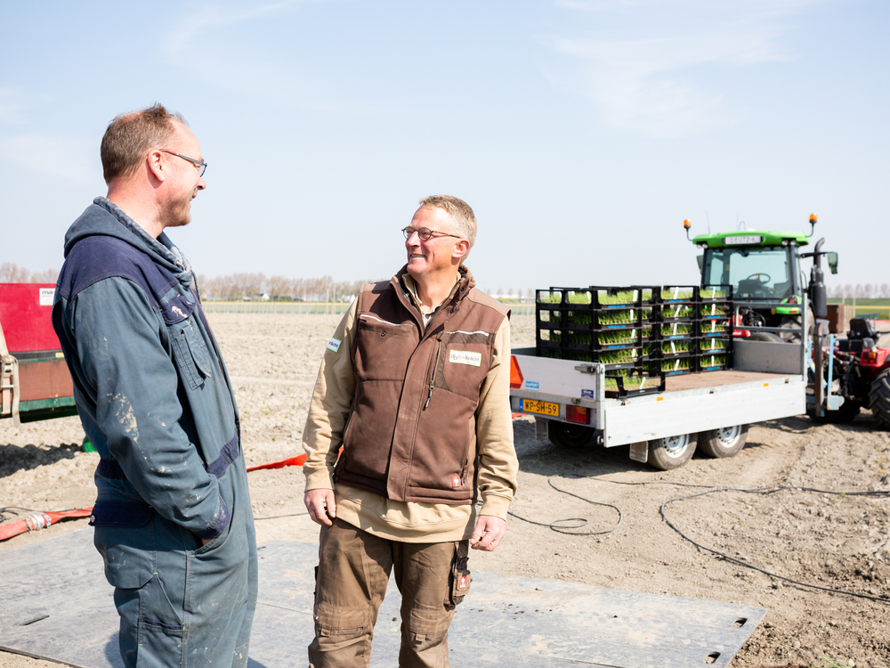 Twee agrarische bedrijfsverzorgers in gesprek naast een tractor op het veld.